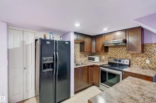 Kitchen featuring wood-finish cabinetry, patterned tile backsplash, and light-toned countertops - 1707 37A Avenue Nw, Edmonton, AB - Indoor Photo Showing Kitchen With Double Sink