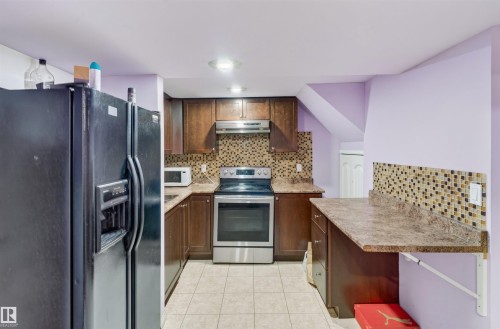 U-shaped kitchen featuring wood-finish cabinetry, tile flooring, mosaic tile backsplash, and stainless steel appliances - 1707 37A Avenue Nw, Edmonton, AB - Indoor Photo Showing Kitchen With Upgraded Kitchen