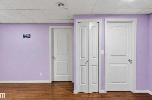 Wood-finish flooring with white baseboards, three white doors, and a ceiling with acoustic panels - 1707 37A Avenue Nw, Edmonton, AB - Indoor