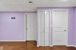 Wood-finish flooring with white baseboards, three white doors, and a ceiling with acoustic panels - 