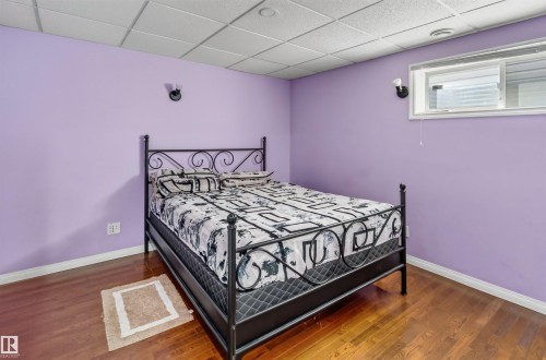 Hardwood-finish flooring with a drop ceiling, wall-mounted sconces, and a window - 1707 37A Avenue Nw, Edmonton, AB - Indoor Photo Showing Bedroom