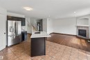 Stainless steel refrigerator, kitchen island with sink and light-toned countertop, dark wood-finish flooring, tiled fireplace with mantel, and recessed lighting - 1707 37A Avenue Nw, Edmonton, AB  - Indoor Photo Showing Kitchen 