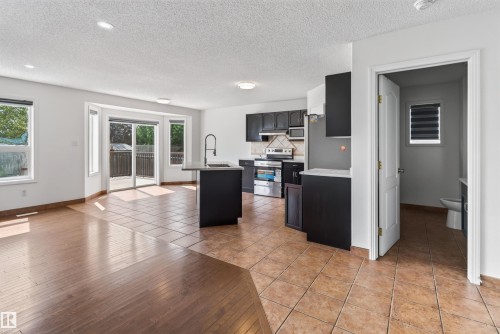 Open-concept living area with wood-finish flooring, a kitchen island with a sink, and sliding glass doors to the outdoor deck - 1707 37A Avenue Nw, Edmonton, AB - Indoor Photo Showing Kitchen