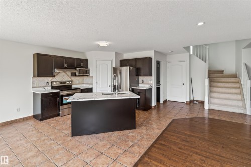 Kitchen with dark wood cabinetry, stainless steel appliances, a center island with a white countertop, and tile flooring - 1707 37A Avenue Nw, Edmonton, AB - Indoor Photo Showing Kitchen