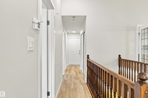 Wood-finish flooring, white walls, and a wood banister with vertical spindles - #21 9375 172 St Nw, Edmonton, AB - Indoor Photo Showing Other Room