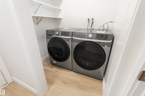 Dedicated laundry area featuring modern front-loading appliances, wood-finish flooring, and integrated shelving - #21 9375 172 St Nw, Edmonton, AB - Indoor Photo Showing Laundry Room
