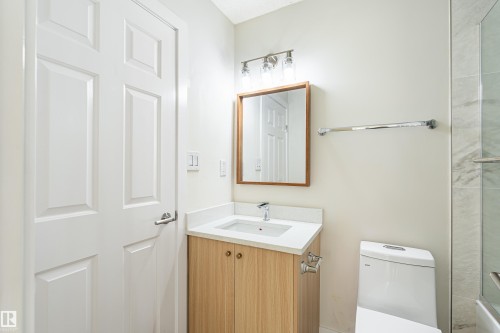 Bathroom featuring a white paneled door, wood-finish vanity with countertop sink, framed mirror, and a toilet - #21 9375 172 St Nw, Edmonton, AB - Indoor Photo Showing Bathroom