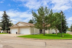 Stucco exterior with an attached two-car garage, concrete driveway, and mature landscaping - 