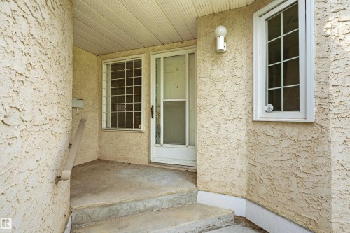 Stucco exterior, covered entryway, white entrance door with storm door, grid-patterned window, and exterior wall-mounted light fixture - #21 9375 172 St Nw, Edmonton, AB - Outdoor With Exterior