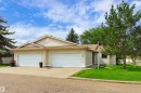 Tan stucco exterior with a brown shingle roof, twin white garage doors, an asphalt driveway, and mature trees - #21 9375 172 St Nw, Edmonton, AB  - Outdoor 