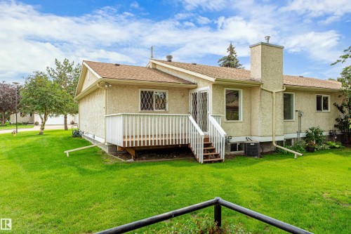 Expansive green lawn surrounds the stucco exterior, featuring a private deck with railing and a substantial chimney - #21 9375 172 St Nw, Edmonton, AB - Outdoor With Deck Patio Veranda