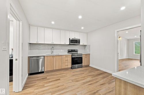 Kitchen featuring wood-finish flooring, two-tone cabinetry, stainless steel appliances, a tile backsplash, and recessed lighting - #21 9375 172 St Nw, Edmonton, AB - Indoor Photo Showing Kitchen With Upgraded Kitchen