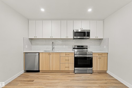 Stainless steel appliances, wood-finish flooring, light wood-finish lower cabinetry, white upper cabinetry, and a tile backsplash - #21 9375 172 St Nw, Edmonton, AB - Indoor Photo Showing Kitchen