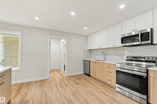 Kitchen featuring wood-finish flooring, two-tone cabinetry, stainless steel appliances, a tile backsplash, and recessed lighting - #21 9375 172 St Nw, Edmonton, AB - Indoor Photo Showing Kitchen