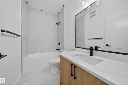 Integrated bathtub and shower with large format wall tiles, vanity with an integrated sink, black-framed mirror, and modern black fixtures - 222 Black Stone Drive Drive, Leduc, AB - Indoor Photo Showing Bathroom