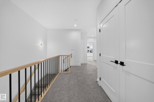 Staircase with wood and metal railing, recessed ceiling lighting, wall-mounted sconce, and white panel doors with matte black hardware - 222 Black Stone Drive Drive, Leduc, AB - Indoor Photo Showing Other Room