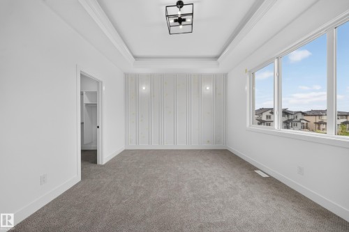 Tray ceiling with a contemporary light fixture, large window, patterned accent wall, and built-in closet shelving - 222 Black Stone Drive Drive, Leduc, AB - Indoor Photo Showing Other Room