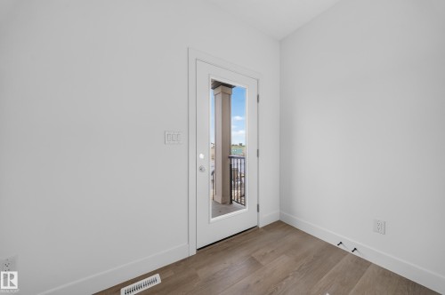 Wood-finish flooring with white baseboards, a full-lite exterior door, and a black metal balcony railing - 222 Black Stone Drive Drive, Leduc, AB - Indoor Photo Showing Other Room