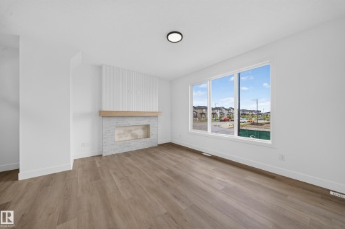 Wood-finish flooring, white walls, large multi-pane window, built-in fireplace with a light-colored stone surround, and wood mantel - 222 Black Stone Drive Drive, Leduc, AB - Indoor Photo Showing Living Room With Fireplace