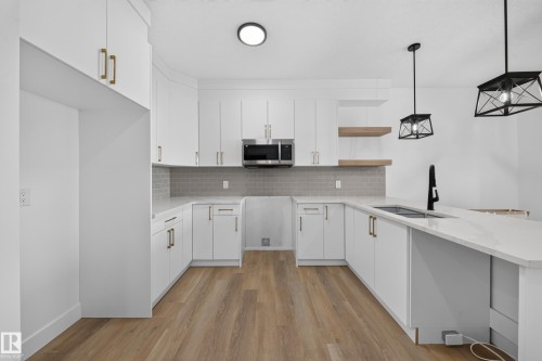 Kitchen featuring white cabinetry with gold-finish hardware, stainless steel microwave, gray subway tile backsplash, white countertops, and wood-finish flooring - 222 Black Stone Drive Drive, Leduc, AB - Indoor Photo Showing Kitchen