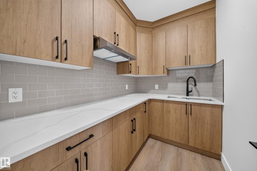 Wood-finish cabinetry with black hardware, white countertops, gray subway tile backsplash, stainless steel range hood, and wood-finish flooring - 222 Black Stone Drive Drive, Leduc, AB - Indoor Photo Showing Kitchen