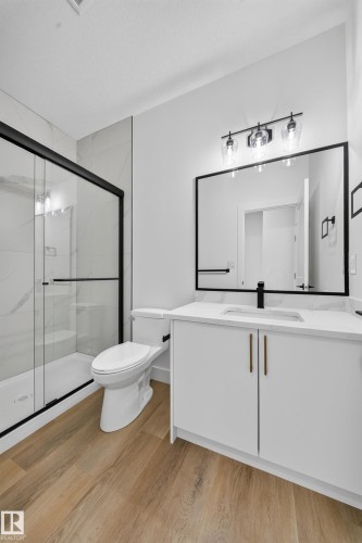Wood-finish flooring, white vanity with integrated sink, black-framed mirror, and a glass-enclosed shower with black trim - 222 Black Stone Drive Drive, Leduc, AB - Indoor Photo Showing Bathroom