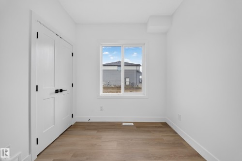 White interior walls with wood-finish flooring, featuring a window and white bi-fold doors with matte black hardware - 222 Black Stone Drive Drive, Leduc, AB - Indoor Photo Showing Other Room