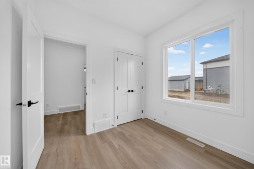 Wood-finish flooring, white trim throughout, white interior doors with matte black hardware, and an expansive window - 222 Black Stone Drive Drive, Leduc, AB - Indoor Photo Showing Other Room