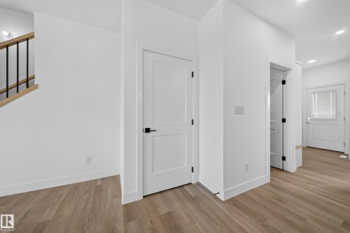 Wood-finish flooring, crisp white walls, contemporary white doors with matte black hardware, recessed lighting, and a modern staircase with a wood handrail and black spindles - 222 Black Stone Drive Drive, Leduc, AB - Indoor Photo Showing Other Room