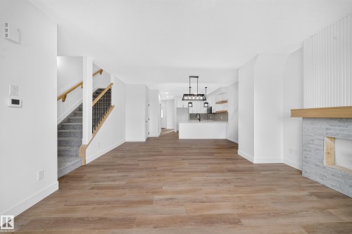 Wood-finish flooring, staircase with carpeted treads and wood handrail, stone fireplace surround with wood mantel, kitchen featuring an island with built-in sink, and pendant lighting - 222 Black Stone Drive Drive, Leduc, AB - Indoor Photo Showing Other Room