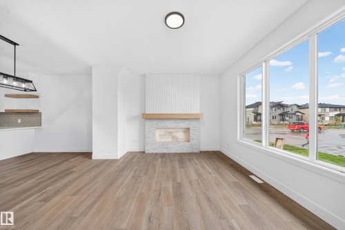 Spacious room featuring wood-finish flooring, a contemporary fireplace with a wood mantle and stone surround, and large windows - 222 Black Stone Drive Drive, Leduc, AB - Indoor Photo Showing Living Room With Fireplace