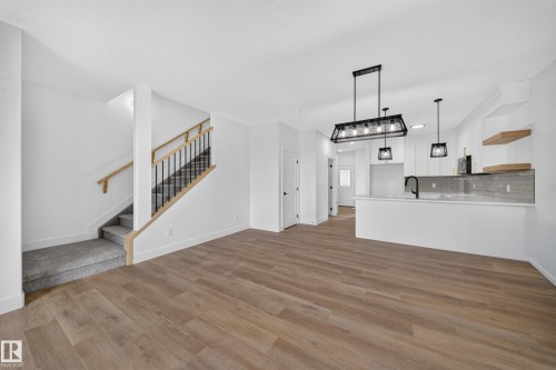 Wood-finish flooring, staircase with wood handrails and black metal balusters, kitchen island with counter seating, subway tile backsplash, and contemporary pendant lighting - 222 Black Stone Drive Drive, Leduc, AB - Indoor Photo Showing Other Room