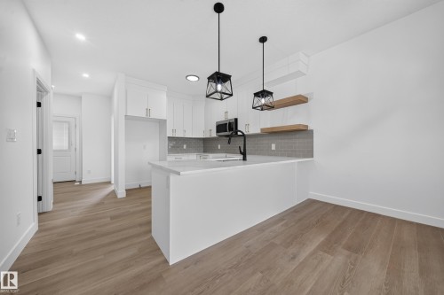 Open concept kitchen with white cabinetry, light countertops, subway tile backsplash, and wood-finish flooring - 222 Black Stone Drive Drive, Leduc, AB - Indoor Photo Showing Kitchen