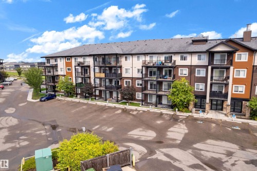 Multi-story building featuring private balconies, a dark shingle roof, and a stone facade entrance - #227 148 Ebbers Bv Nw, Edmonton, AB - Outdoor With Balcony With Facade