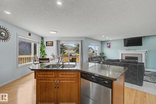 Kitchen island with stone countertop, integrated dishwasher, and wood cabinetry - 3236 21 Street Nw, Edmonton, AB - Indoor Photo Showing Kitchen With Fireplace With Double Sink