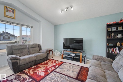 Vaulted ceiling, track lighting, large window with grid pattern, light blue accent wall, built-in shelving unit - 3236 21 Street Nw, Edmonton, AB - Indoor Photo Showing Living Room