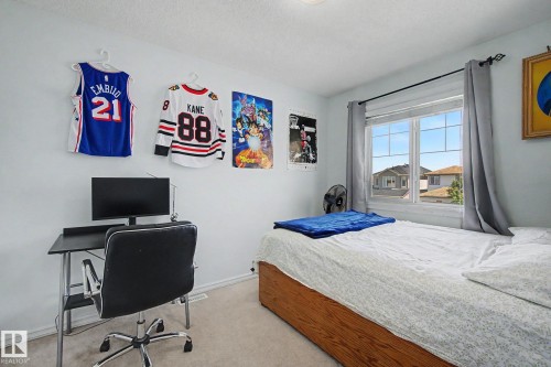 Carpeted bedroom featuring a large window with curtain rod, wood-finish bed frame, and light-colored walls - 3236 21 Street Nw, Edmonton, AB - Indoor Photo Showing Bedroom