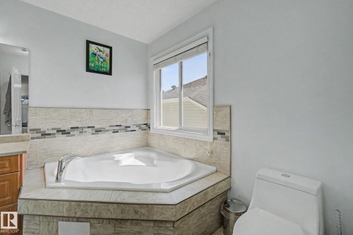 Corner soaking tub with deck-mounted chrome faucet, tiled surround, and decorative mosaic accent - 3236 21 Street Nw, Edmonton, AB - Indoor Photo Showing Bathroom