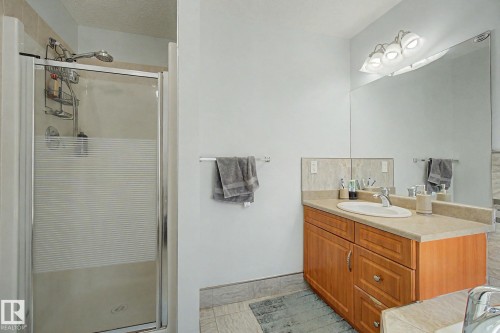 Walk-in shower with sliding glass door, single vanity with wood-finish cabinetry, countertop, and large wall-mounted mirror - 3236 21 Street Nw, Edmonton, AB - Indoor Photo Showing Bathroom