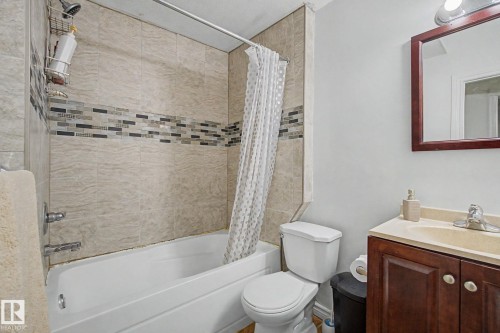 Bathtub with tiled surround featuring a decorative mosaic accent band - 3236 21 Street Nw, Edmonton, AB - Indoor Photo Showing Bathroom