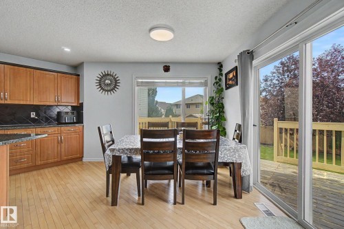 Wood-finish flooring, light wood cabinetry, dark tile backsplash, dark-toned countertop, and sliding glass doors to outdoor decking - 3236 21 Street Nw, Edmonton, AB - Indoor Photo Showing Dining Room