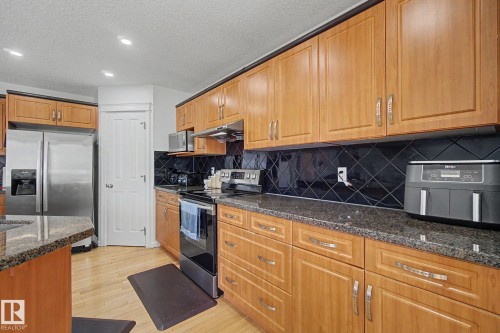 Kitchen featuring wood cabinetry, stainless steel appliances, dark stone countertops, and black tile backsplash - 3236 21 Street Nw, Edmonton, AB - Indoor Photo Showing Kitchen