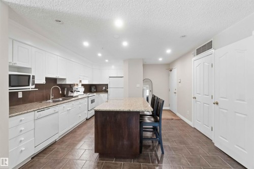 Kitchen featuring white cabinetry, light-toned countertops, a dark-toned island, and tile flooring - #104 10221 111 St Nw, Edmonton, AB - Indoor Photo Showing Kitchen With Double Sink