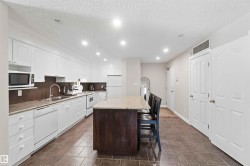 Kitchen featuring white cabinetry, light-toned countertops, a dark-toned island, and tile flooring - 