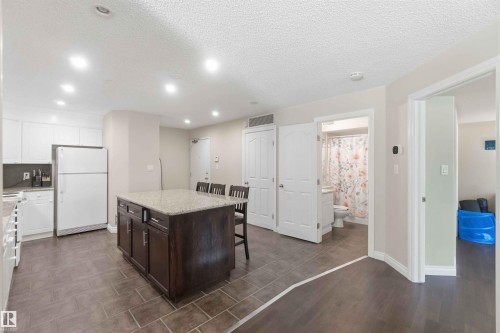 Open-concept kitchen and dining area featuring a dark wood-finish island with seating, white cabinetry, stainless steel appliances, and recessed ceiling lighting - #104 10221 111 St Nw, Edmonton, AB - Indoor Photo Showing Kitchen