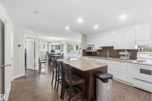 Kitchen featuring white cabinetry, brown tile backsplash, white appliances, and a central island with a stone countertop - #104 10221 111 St Nw, Edmonton, AB - Indoor Photo Showing Kitchen