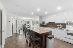 Kitchen featuring white cabinetry, brown tile backsplash, white appliances, and a central island with a stone countertop - 