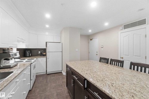 Kitchen featuring white cabinetry, a built-in range, a double-door refrigerator, and a center island with a stone-finish countertop - #104 10221 111 St Nw, Edmonton, AB - Indoor Photo Showing Kitchen