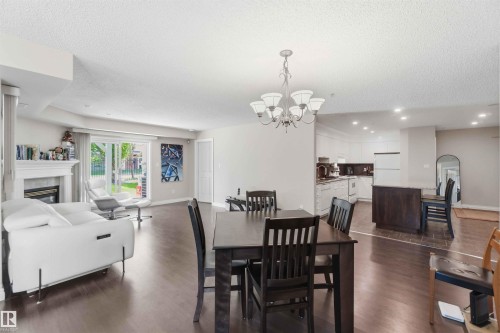 Wood-finish flooring, white fireplace with mantle, sliding glass patio door, recessed lighting, and kitchen island with seating - #104 10221 111 St Nw, Edmonton, AB - Indoor Photo Showing Dining Room With Fireplace