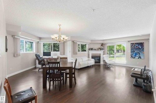 Spacious interior featuring wood-finish flooring, multiple windows, a decorative chandelier, and a built-in fireplace with a mantel - #104 10221 111 St Nw, Edmonton, AB - Indoor Photo Showing Other Room With Fireplace